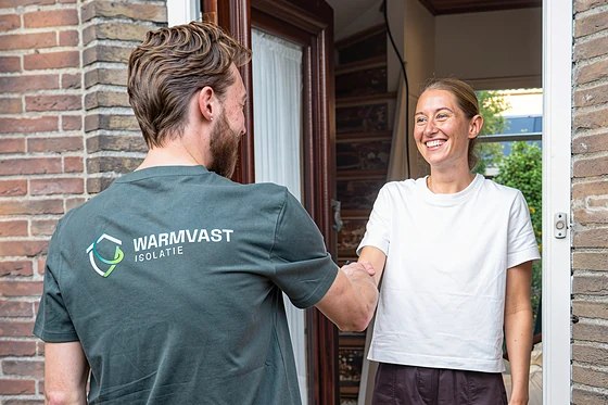 Warmvast-monteur geeft een bewoner een hand bij de voordeur, aan het begin van de technische opname